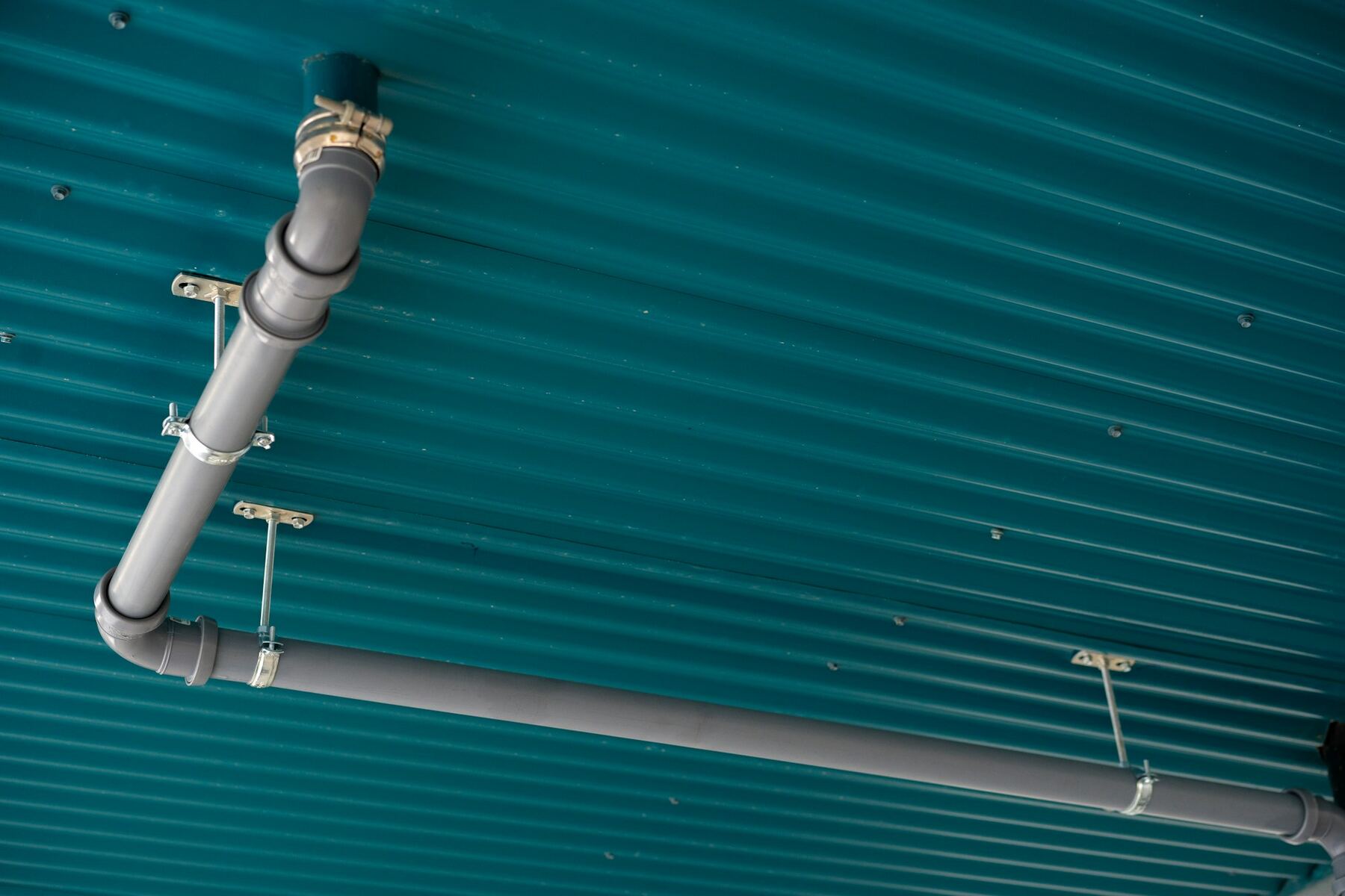 A pipe run fixed to a teal ribbed ceiling